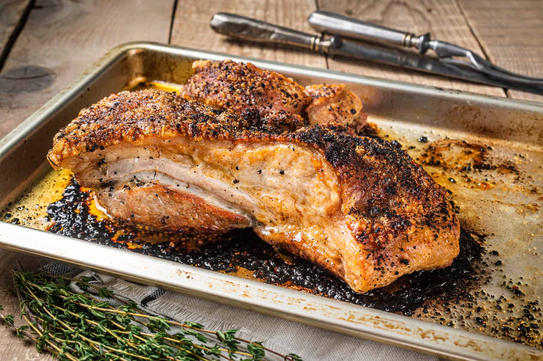 Zwei knusprig gegrillte Schweinebauchstücke mit Gewürzkruste auf Backblech mit Thymian