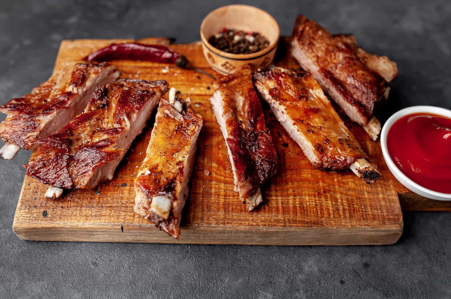 Gegarte Spareribs in Scheiben geschnitten auf Holzbrett mit BBQ-Sauce und Gewürzen