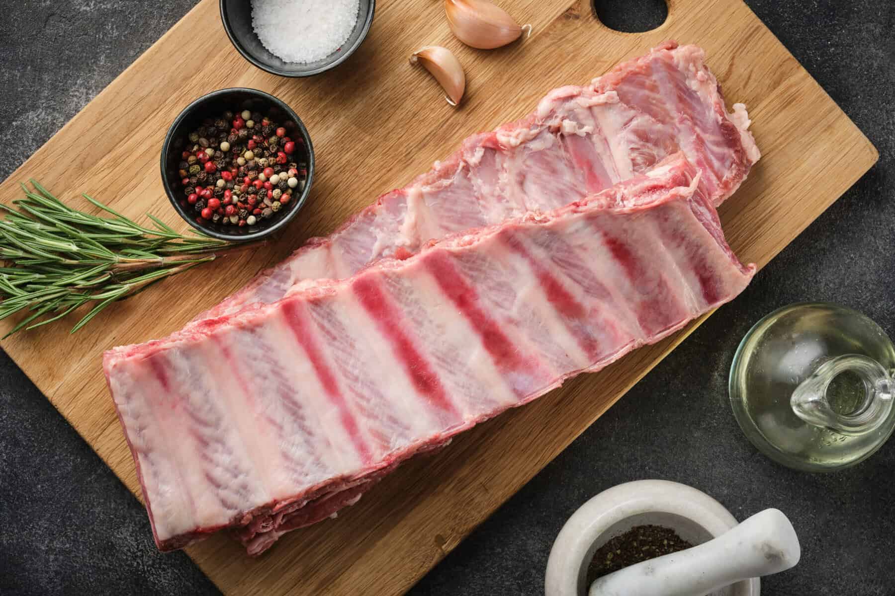 Rohe Spareribs mit Pfeffer, Salz und Rosmarin auf Bambusschneidebrett