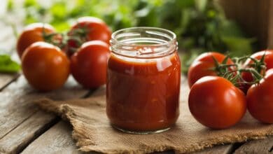 Einmachglas mit rotem Ketchup umgeben von frischen Tomaten auf Jutestoff