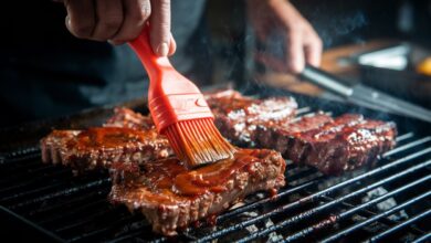 Grillmeister trägt Korean BBQ-Sauce auf Short Ribs auf, Flammen im Hintergrund